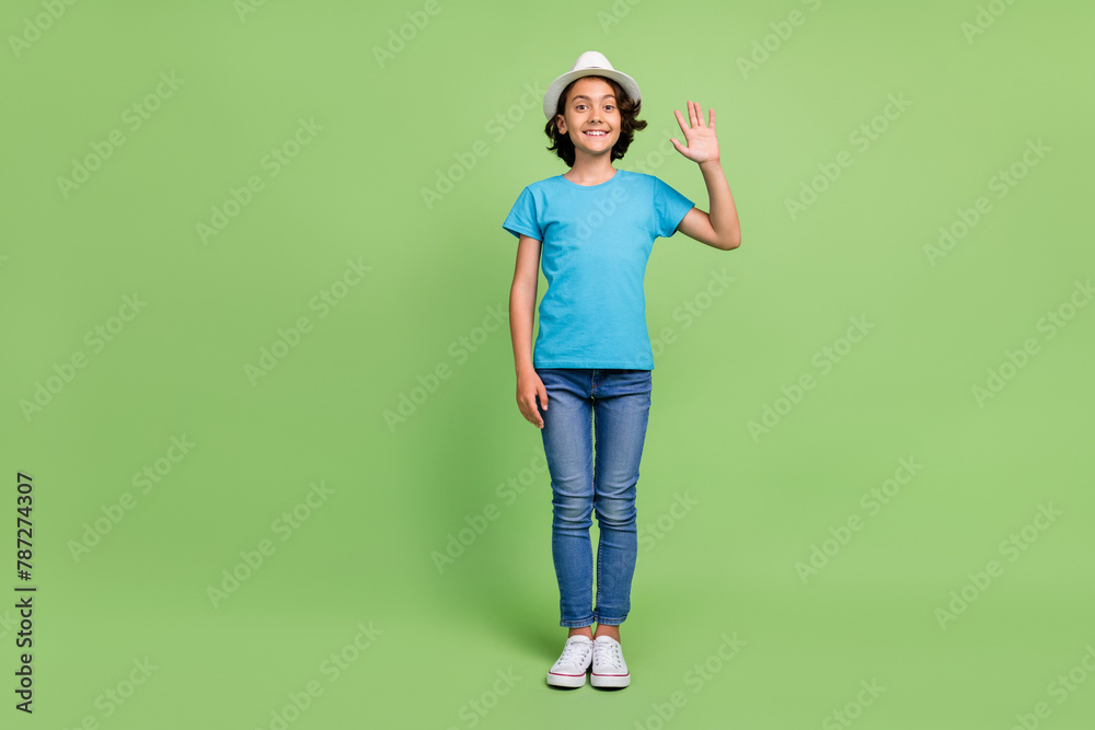 Full length photo of friendly excited boy wear t-shirt waving arm hi emtpy space isolated green color background Full length photo of friendly excited boy wear t-shirt waving arm hi emtpy space isolated green color background