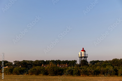 A beautiful white and red lighthouse on the North Sea coast in the Netherlands. Lighthouse against the blue sky. Beautiful metal construction.