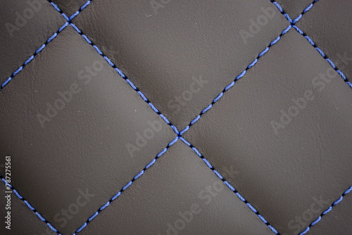 Blue contrast thread extreme close-up on a dark gray leather car seat