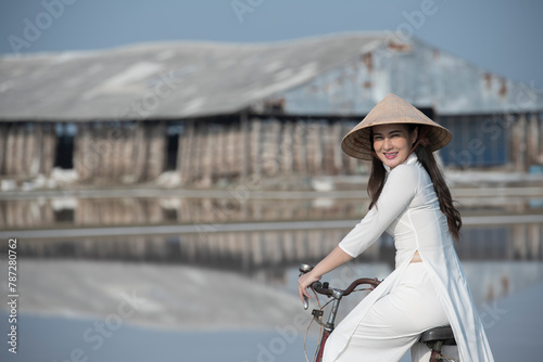 Beautiful Vietnamese Asian woman wearing a blue color Ao Dai National Costume Dress with red bicycle and flowers fresh yellow rice fields and mountain background. Portrait fashion show in nature.