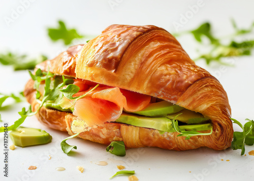 Croissant sandwich with salmon and avocado on the white table