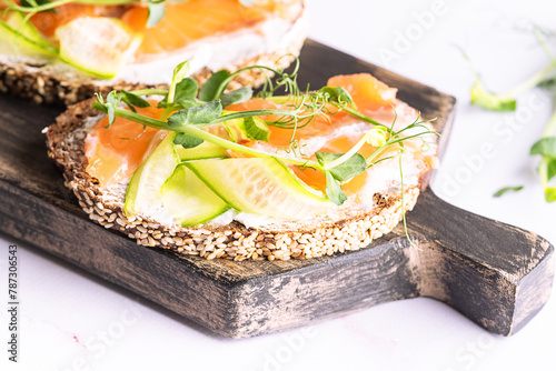 Salmon sandwiches with fullgrain bread, pea micro greens, cream cheese and cucumbers on white marble background close up.
 photo