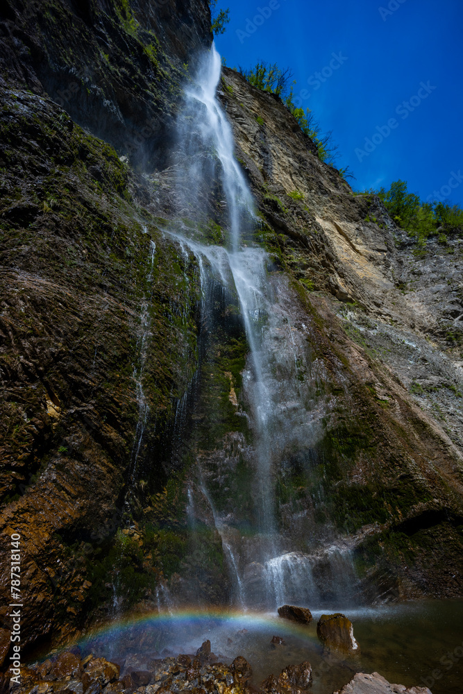 Fototapeta premium Waterfall hidden inside the forest, beauties of Slovenia to be discovered. Near Nova Gorica, Tolmin village. Water spray and vivid rainbow forms from the waterfall that falls sheer onto the rock.