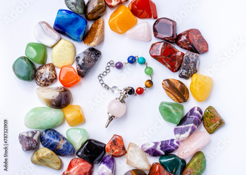 Pendulum made of natural stones (rose quartz) against the background of semi-precious multi-colored stones.