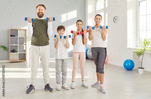 Family strength training. Cheerful active family with kids lifting dumbbells together in their bright and modern home gym. Father, mother, son and daughter ready for sports training. Sports concept.