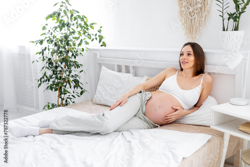 A pregnant woman with a big open belly on a bed at home dreams of having a baby. The expectant mother is waiting and preparing for the birth of a child in a bright bedroom