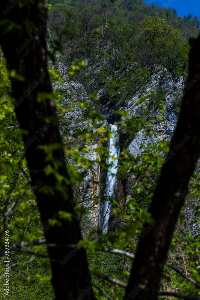 Fototapeta premium Gregorčičev Waterfall hidden inside the forest, beauties of Slovenia to be discovered. Near Nova Gorica, Tolmin village. Water spray, vivid rainbow forms from the waterfall that falls onto the rock.