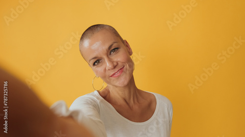 Close-up, young hairless woman taking selfie looking at camera isolated on yellow background in studio