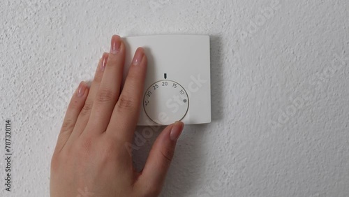 Female hand turns on central Heating thermostat, control dial adjustment. Stops at 20 degree Celsius. Saving money and electricity