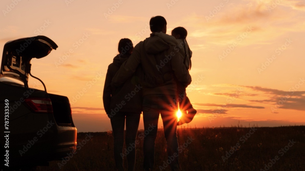 Silhouettes of happy family at sunset near car. Dad mom and girl kid watching contemplating setting sun, orange stunning summer sky. Solitude of family in nature, break from hustle and bustle of city - obrazy, fototapety, plakaty 