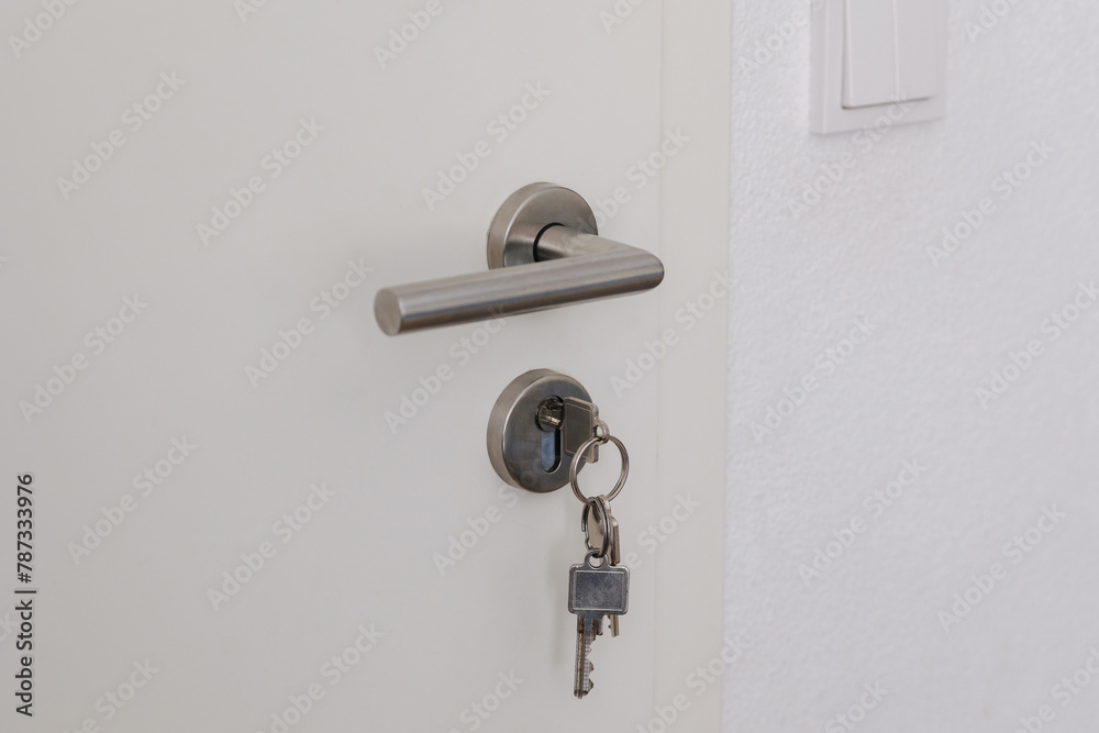 Closed door with keys in the lock. White door and metal handle