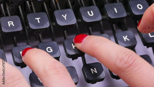 fingers with red nail polish of the young woman typing the keys on the keyboard of the vintage typewriter in the office photo