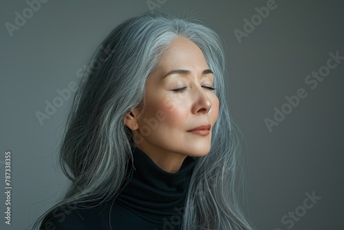 An Asian woman appears reflective with eyes closed, wearing black and posed against a gray background photo
