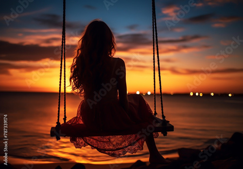 Romantic silhouette detail of a woman on a swing on the beach at sunset photo