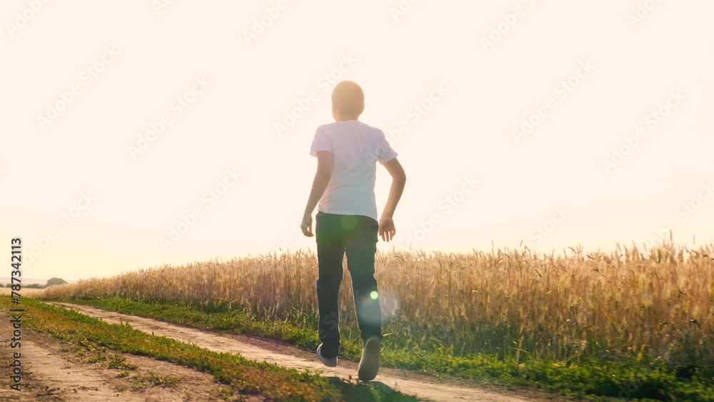 Cheerful teen boy running on dirt road at sunny sunset sunrise wheat field enjoy freedom happy childhood. Male kid teenager speed movement outdoor leisure activity at summer autumn rye meadow - obrazy, fototapety, plakaty 