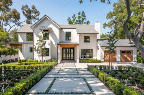A white craftsman style home with large windows and black trim. An extra wide driveway in front of the house has concrete pavers with green grass between them and square ornamental hedges © Kien