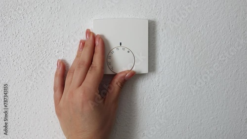 Woman turning down heating thermostat to save money. Female turn off heating. Central Heating thermostat control dial adjustment