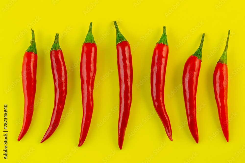 A row of red peppers are lined up on a yellow background. The peppers are all different sizes and are arranged in a straight line. A row of red peppers are lined up on a yellow background. The peppers are all different sizes and are arranged in a straight line.
