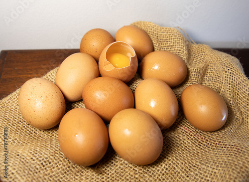 brown eggs on burlap, one egg is broken and the yolk is visible. Kitchen background