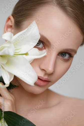 Delicate fashion beauty portrait of a beautiful girl with lily flowers isolated on a gray background.