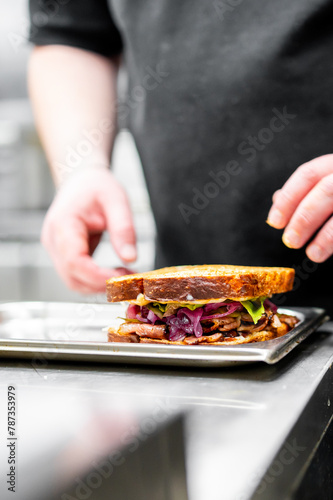 Professional chef meticulously preparing a gourmet sandwich with fresh ingredients in a well-lit kitchen