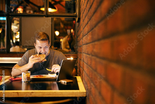 Man eating burger in restaurant and watching videos on tablet.