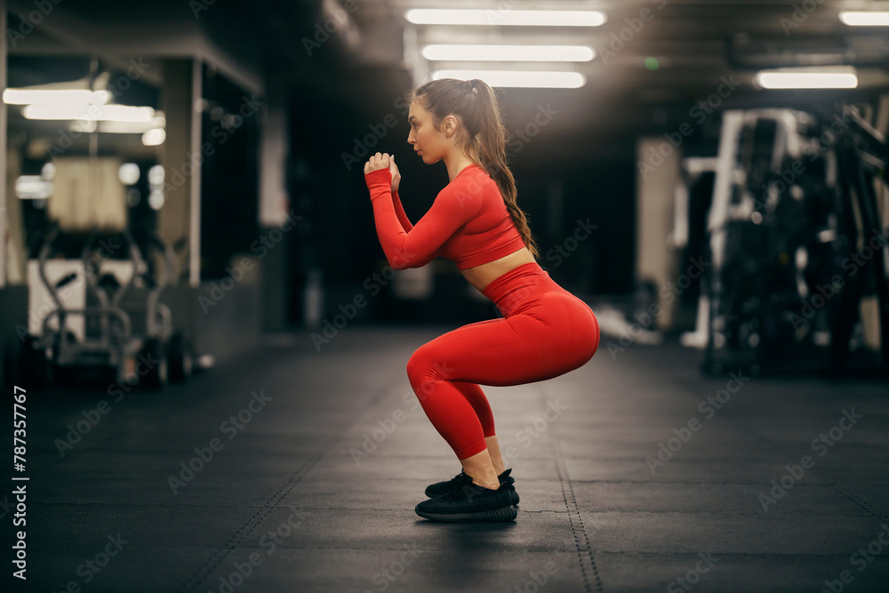 Obraz premium Side view of a fit sportswoman doing squat endurance in a gym.