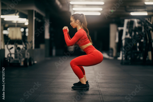 Side view of a fit sportswoman doing squat endurance in a gym.