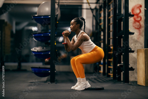 Side view of a black strong sportswoman exercising with weights in a squat position. photo