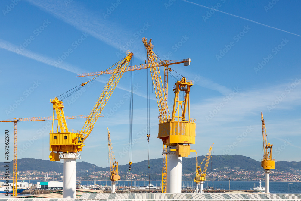 This image showcases several large yellow industrial cranes towering over a construction site with a clear blue sky This image showcases several large yellow industrial cranes towering over a construction site with a clear blue sky