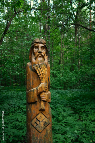 ritual wooden pagan idol in forest  abstract natural green background. old god totem in traditional Slavic folk style. bearded old man with wheat in his hands. Attribute of pagan religious rites.