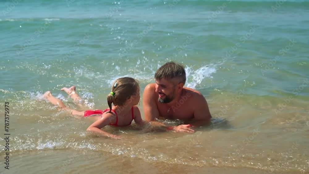 Father and little daughter lie on seashore in water and funny swim in waves in summer day. Happy family with child on vacation. Travel, holiday, tourism Father and little daughter lie on seashore in water and funny swim in waves in summer day. Happy family with child on vacation. Travel, holiday, tourism