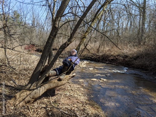 A man lays on a tree in the forest beside a creek on a sunny day in the spring
