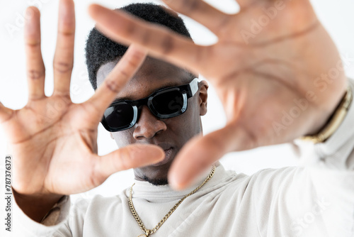 A black man wearing sunglasses is gesturing with his hand in a studio setting against a white background.