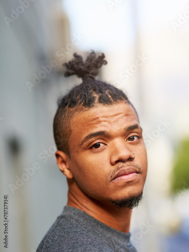 Portrait, black man and cool or funky hairstyle in city with topknot and braided hair for barbershop. Creative, unconventional and serious african person, face or identity expression with urban style photo