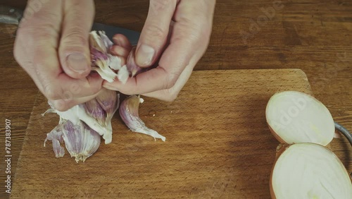Woman's hands close up cutting onion and smashing, and peeling garlic on a wooden board with a big knife. Wooden kitchen table. . High quality 4k footage