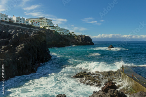 Resort hotel on a rocky shore and the blue water of the ocean. Charco de Isla Cangrejo Santiago Del Teide, Tenerife island, Spain. Los Gigantes. Natural swimming pool with foamy waves, sunbathe spot