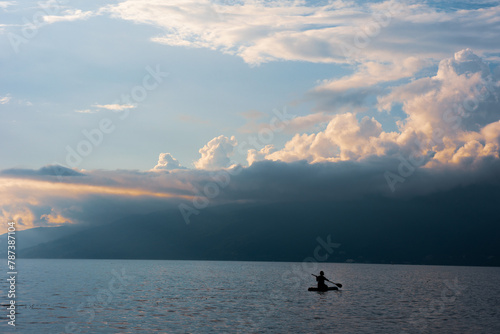 A man is kayaking on a lake with a cloudy sky in the background