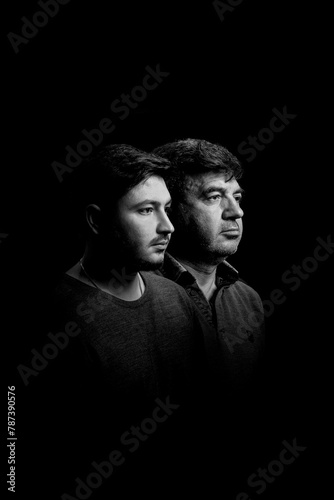 Commemorative black and white portrait photo of middle-aged father and his teenage son side by side. Father and son look alike.