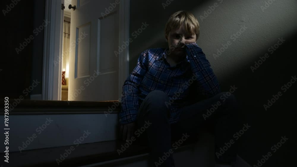Abused boy sits in the dark and looks at the camera in a family home Abused boy sits in the dark and looks at the camera in a family home