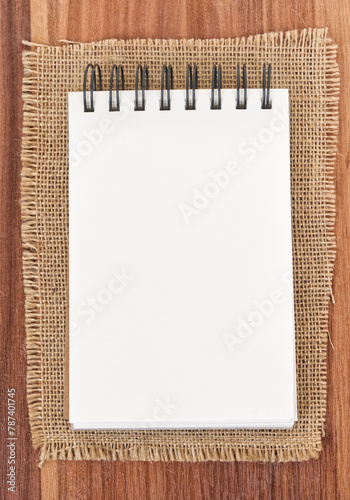 Notepad on jute burlap - wooden background. Notepad on white background - top view.