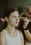A young makeup artist applies blush to a girl s cheeks.
