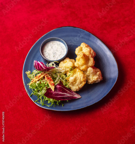 Portion of battered cauliflower appetizer with greens and sauce