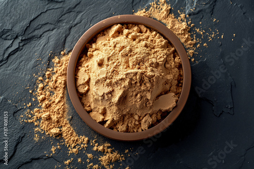 A bowl of maca powder on a textured black slate surface, with some powder sprinkled around