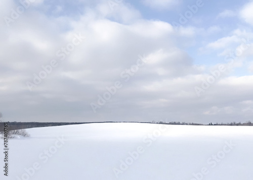 A small rise in a snow covered pasture topped by a sky of fluffy, white clouds creating a white on white landscape