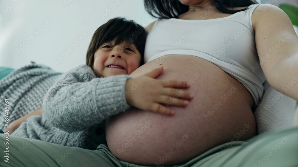 Happy small 5 year old boy gently rubs mother's pregnant belly during late stage of pregnancy. Happiness maternal concept between loving genuine family moment Happy small 5 year old boy gently rubs mother's pregnant belly during late stage of pregnancy. Happiness maternal concept between loving genuine family moment