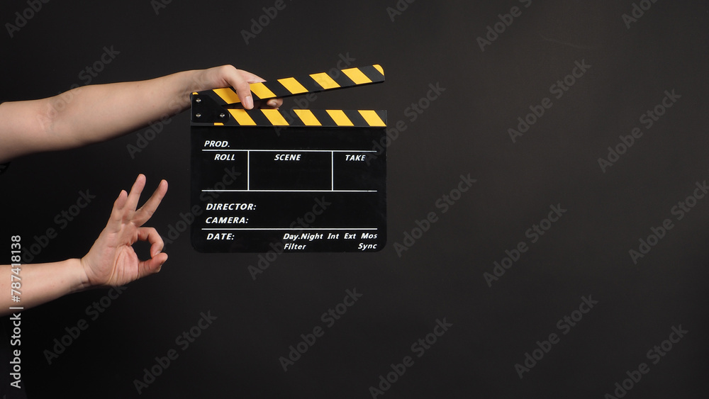 hands is holding the clapper board an do ok han sign on black background.
