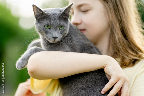 Cute teenage girl holding her pet cat on sunny summer day. Gorgeous grey Russian Blue breed cat outdoors. © MNStudio