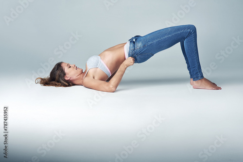Studio, fashion and woman with jeans for getting ready, dressing and challenge on grey background. Female person, denim and tight pants with struggle for weight gain, diet and stretching on floor