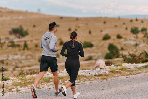 A couple dressed in sportswear runs along a scenic road during an early morning workout, enjoying the fresh air and maintaining a healthy lifestyle